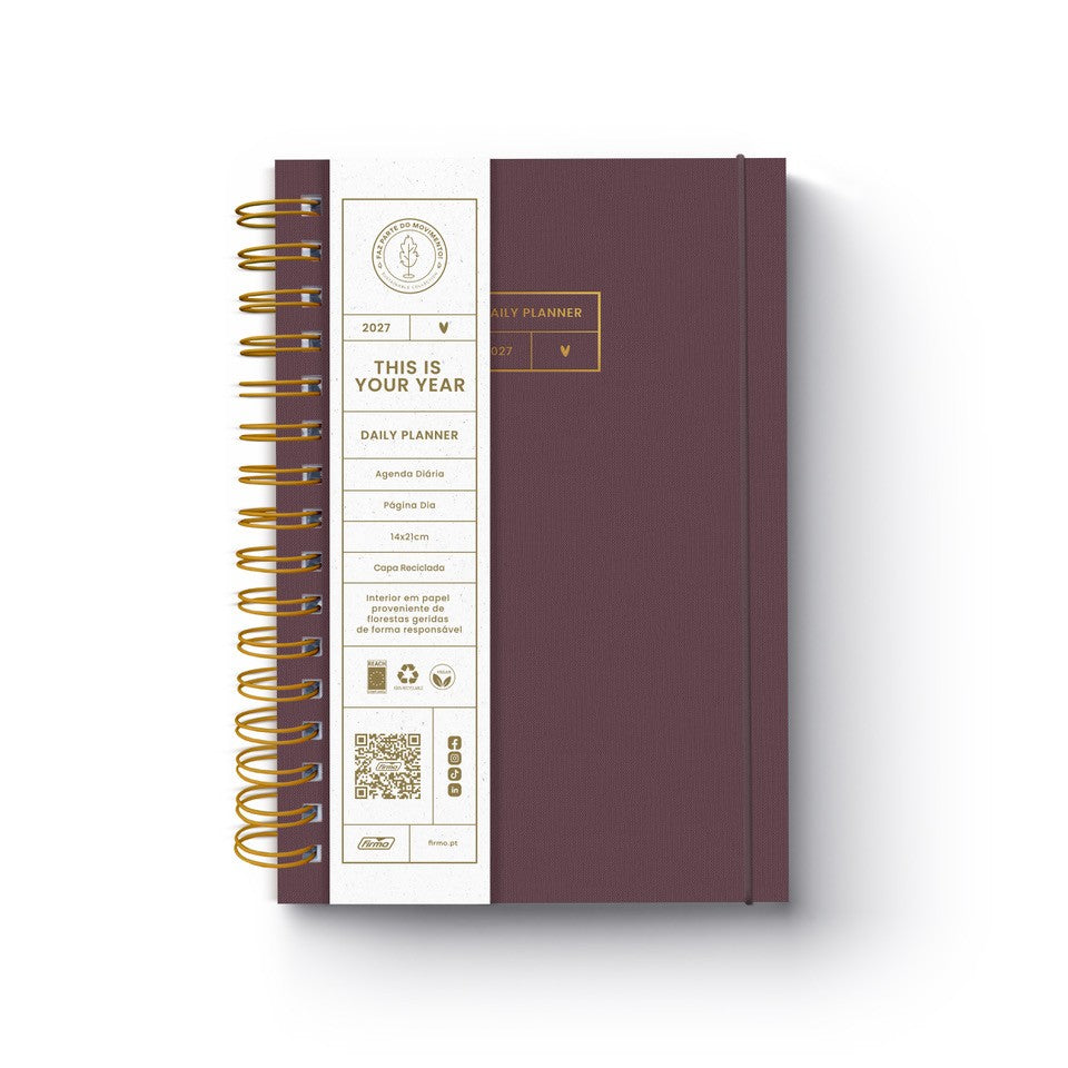 Agenda diária de 2027 Eco Elle da Firmo, em tom bordeaux texturado com gravação dourada "this is your year", encadernação em espiral bronze e uma faixa protetora branca com especificações ecológicas, sobre fundo branco.
