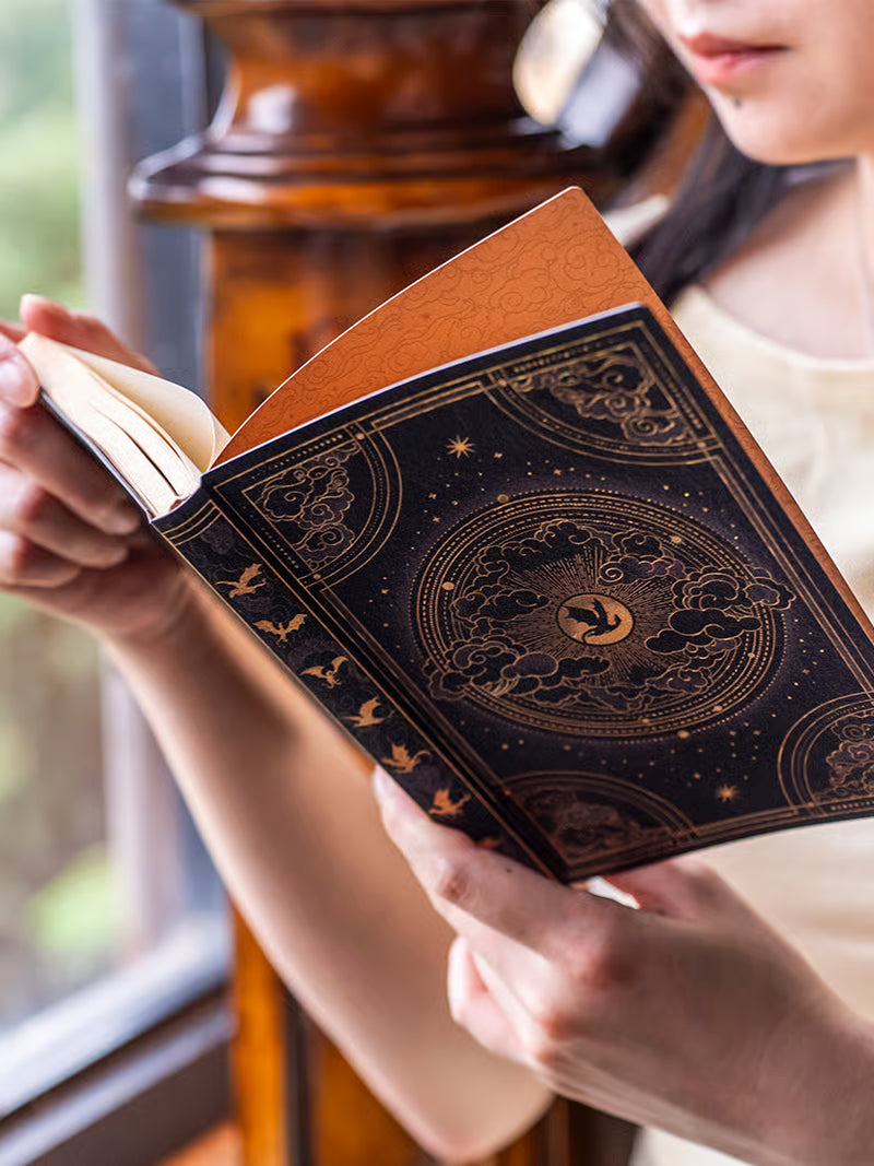 Agenda de capa preta com desenho dourado segurada por mãos, com emblema central