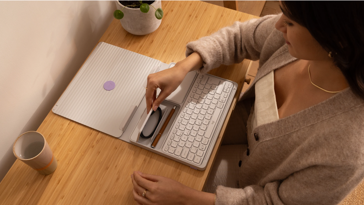 Secretária pop-up com teclado e touchpad cinzenta, em uso numa mesa